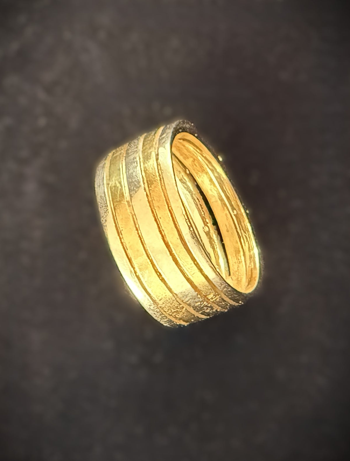 A gold ring with multiple concentric textured bands, photographed against a dark textured background.
