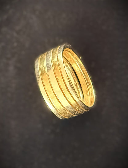 A gold ring with multiple concentric textured bands, photographed against a dark textured background.